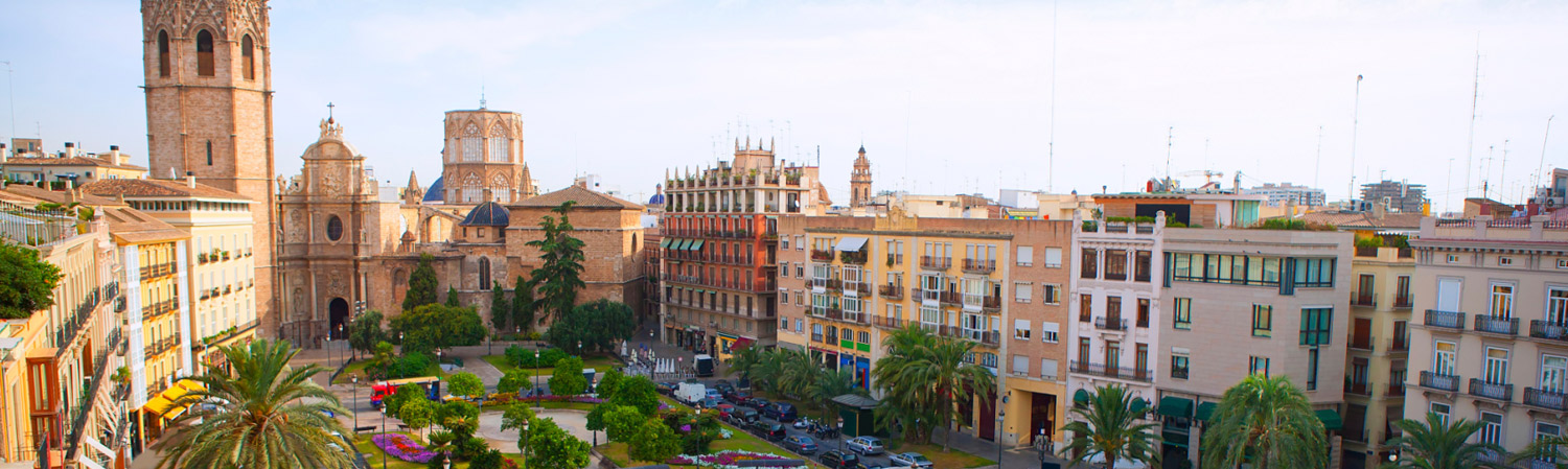 Vista panorámica de una plaza histórica europea con una torre de catedral ornamentada, edificios de tonos crema y arenisca, y ambiente tranquilo al atardecer
